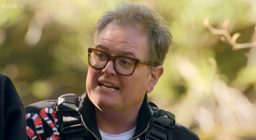 Alan Carr wearing glasses and a black jacket with a red and white sequined snake design.