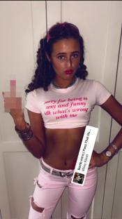 Tyson Fury's daughter giving the middle finger while wearing a pink shirt that says "sorry for being so sexy and funny idk what's wrong with me" and pink ripped jeans.