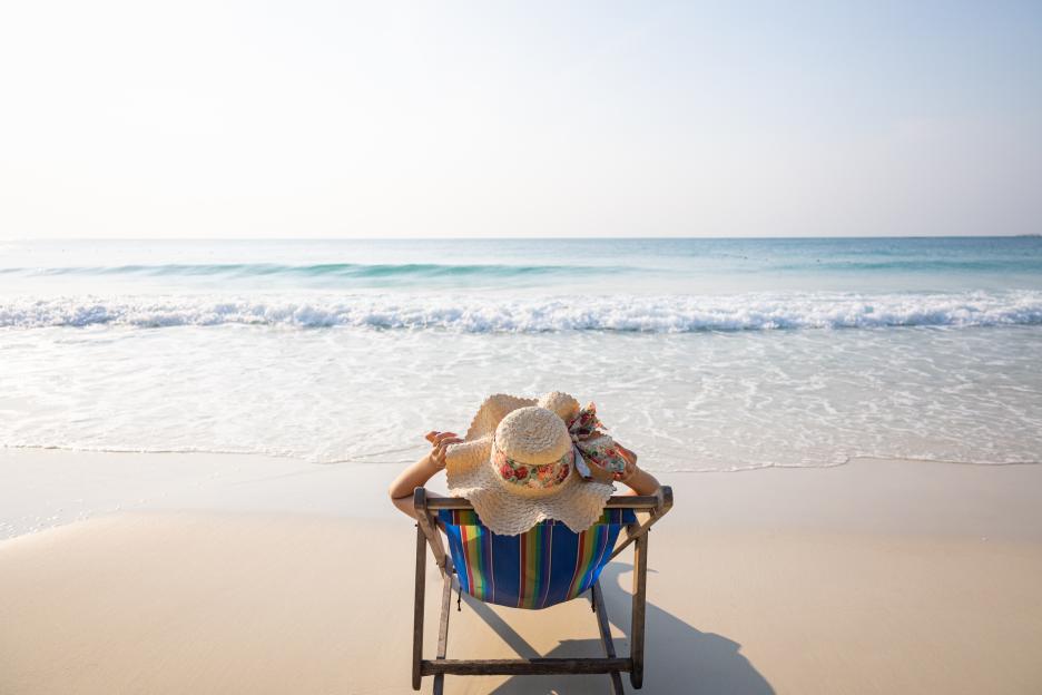 Woman relaxing in a beach chair on the sand, facing the ocean.