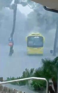 A yellow bus driving through a flooded street during a heavy rainstorm.