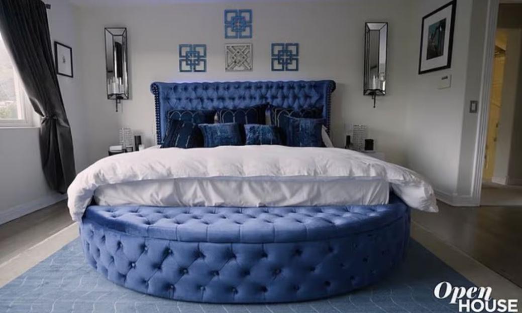 A bedroom featuring a large bed with a blue tufted headboard and matching circular ottoman.