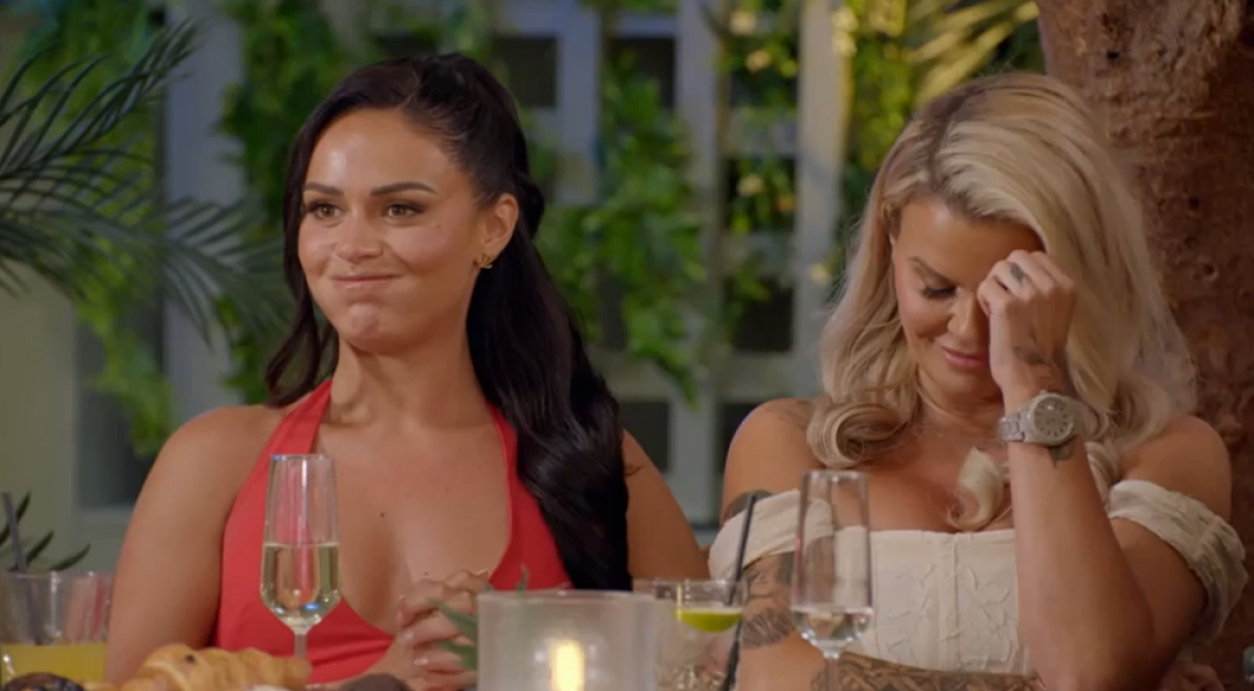 Two women sitting at a table, one looking unimpressed, the other wiping away tears.