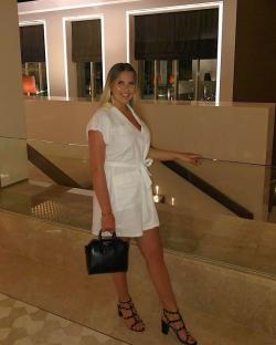 Woman in white dress and black heels posing in a hotel.