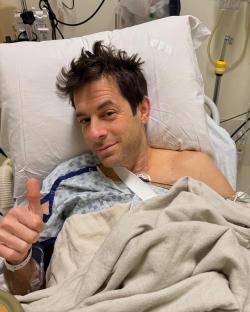 Mark Ronson in a hospital bed giving a thumbs-up.