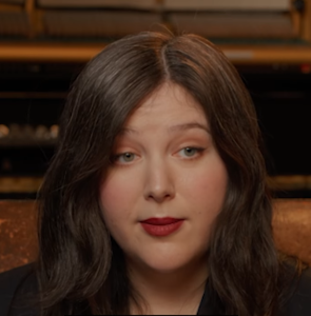 A woman with long dark hair, parted in the middle, wearing dark lipstick.