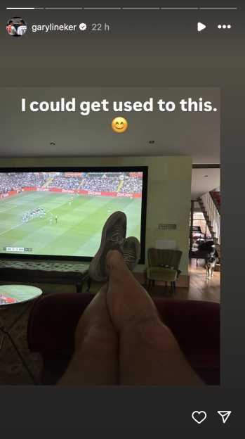 Screenshot of a person's legs up on a chair in front of a large screen showing a soccer game.