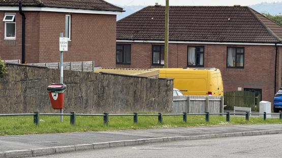Photo of a dog waste bin on a street near houses.