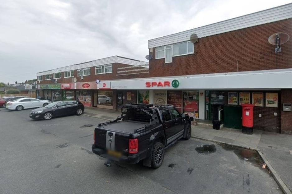 A row of brick buildings with shops, including a Spar grocery store, and a red mailbox outside.