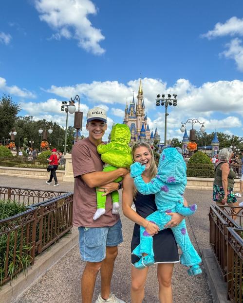 Abby and Matt Howard hold two children dressed as Mike and Sulley from Monsters, Inc. in front of Cinderella Castle at Magic Kingdom.