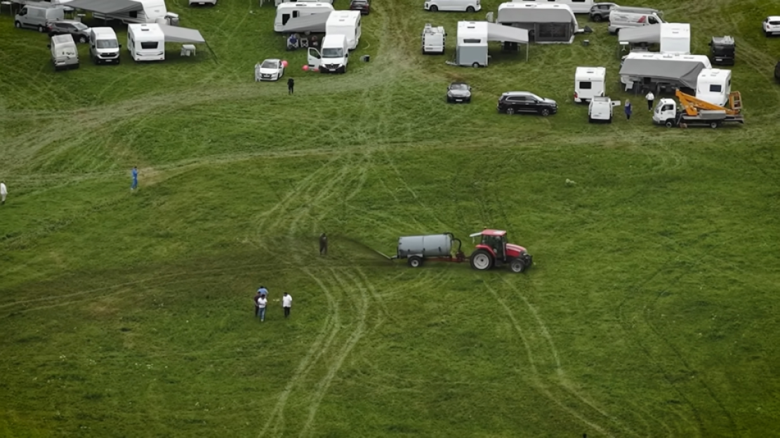 Aerial view of a tractor spreading fertilizer on a field with RVs parked nearby.