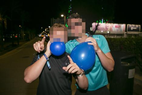 Two people inflating blue balloons at night.