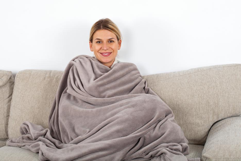 Blonde woman wrapped in a grey blanket on a sofa.