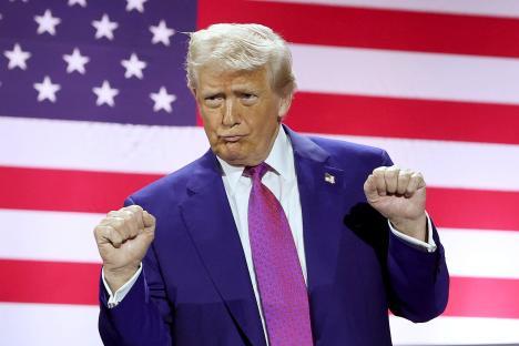 Donald Trump gesturing with fists clenched in front of an American flag.