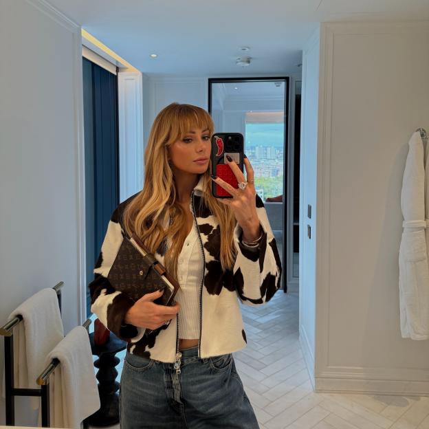 Olivia Attwood taking a mirror selfie in a cow print jacket, white top, and jeans, holding a Louis Vuitton planner.