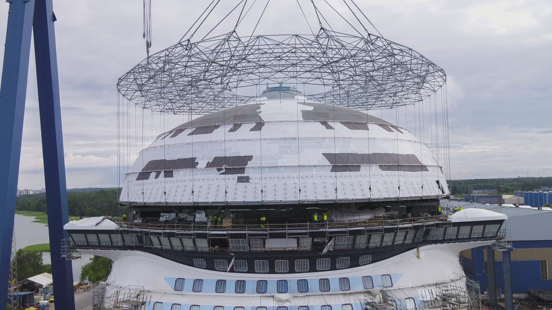 A crane lifts a dome-shaped structure onto the Legend of the Seas cruise ship during construction.