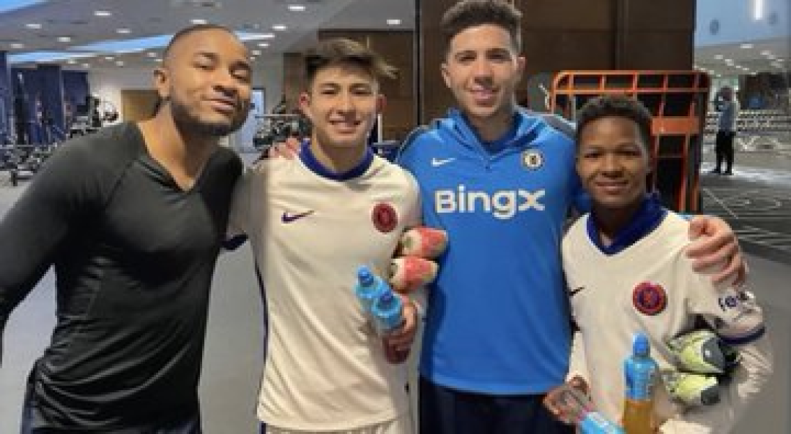 Four men posing for a photo, two in Chelsea FC jerseys.