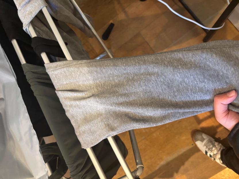 A hand holds a gray shirt to show it drying on a heated clothes airer, with a shoe and wooden floor visible below.