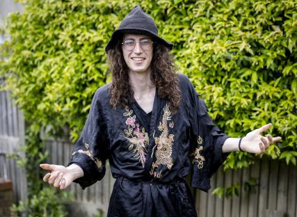 Man with long curly hair, glasses, and a black robe with gold embroidery, smiles and gestures with his hands.