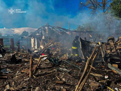 Firefighters surveying the damage to a destroyed building and vehicle.