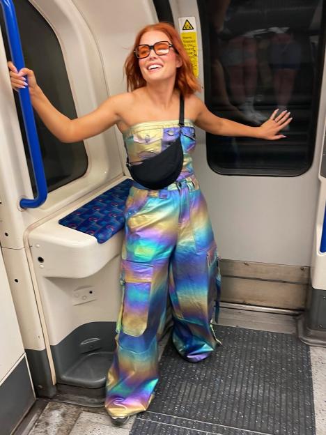 A smiling woman in an iridescent outfit on a subway.