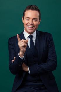 Stephen Mulhern in a suit, gesturing with his index finger.