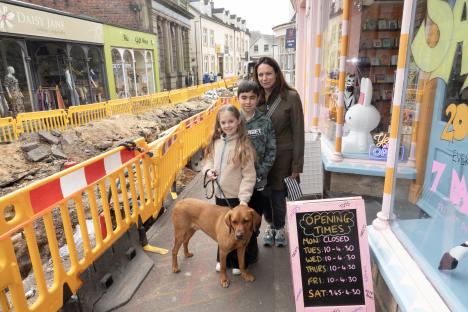 A family with a dog stands outside a shop in Nailsworth, Gloucestershire, near a damaged gas main.