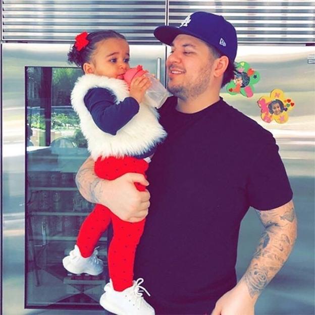 Rob Kardashian holds his daughter, Dream Kardashian, who is drinking from a bottle.