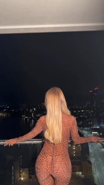 Jess Gale modeling a leopard-print bodysuit on a balcony at night.