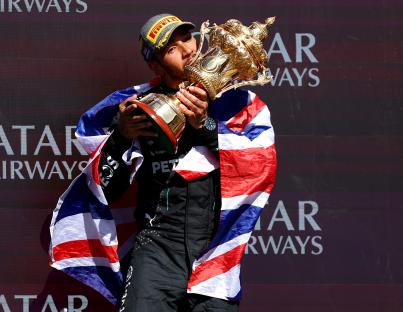 Lewis Hamilton kissing a trophy while draped in a Union Jack.