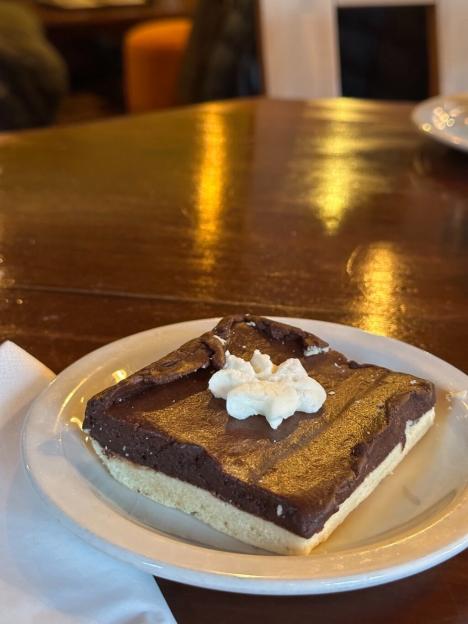 A square chocolate dessert with a dollop of whipped cream on a white plate.