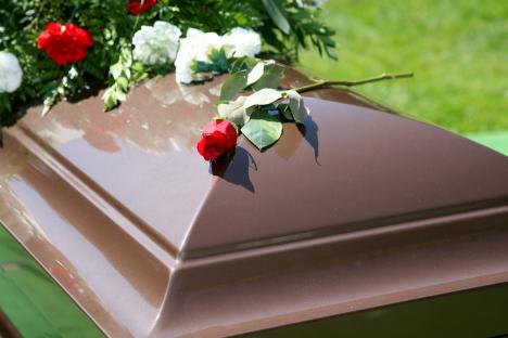 A single red rose on a brown casket.
