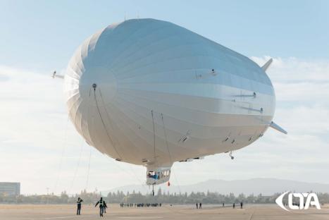 Large white airship on a tarmac with ground crew.
