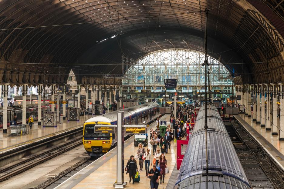 Paddington railway station in London, showing a train on the tracks and many people on the platforms.