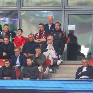 Harry Kane, FC Bayern München executives, and others in the stands at a Bundesliga match.