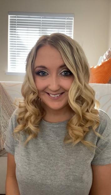 A blonde woman with curly hair smiles at the camera.