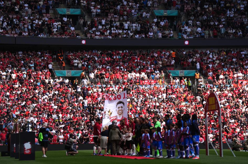 Liverpool and Crystal Palace players line up before a match, with a banner honoring Diogo Jota visible in the crowd.
