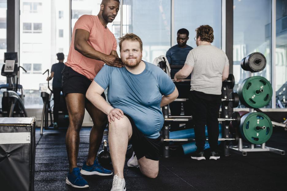 Fitness instructor assisting an overweight man in a gym.