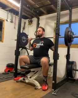 Man performing a barbell shoulder press in a home gym.