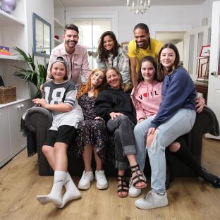Group photo of eight people, including children and adults, sitting on a couch.