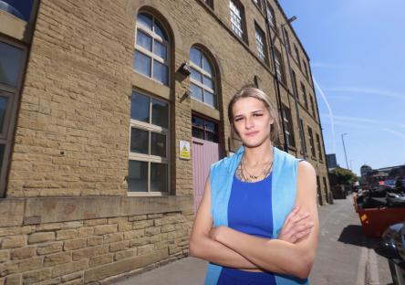 Woman standing in front of a brick building, arms crossed.