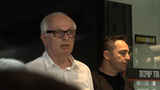 A man in glasses speaks to the camera.