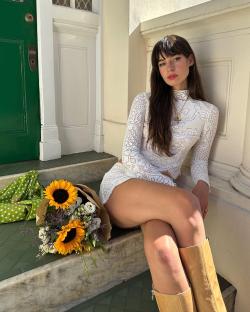 Woman in white lace outfit sitting on steps with sunflowers.