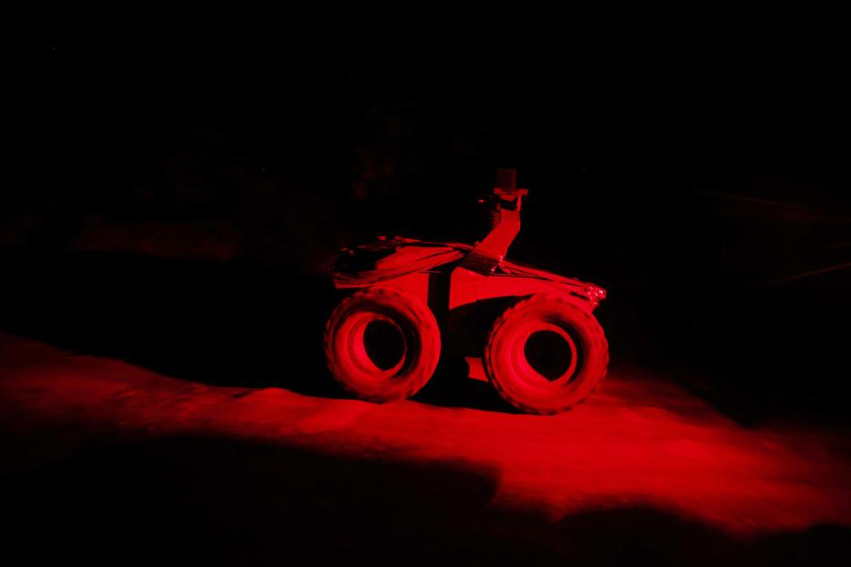 Unmanned ground vehicle (UGV) in a dark area illuminated by red light.