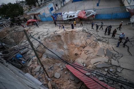 Destroyed courtyard of a hospital in Khan Yunis, Gaza, with people walking amidst the rubble.