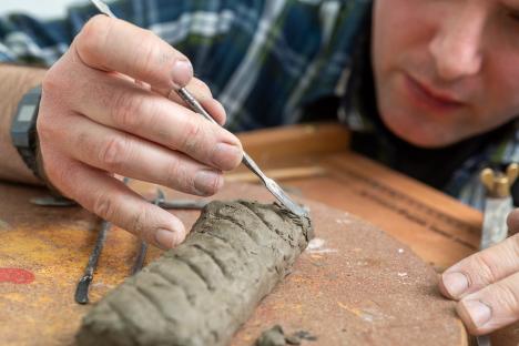 Person sculpting clay with tools.