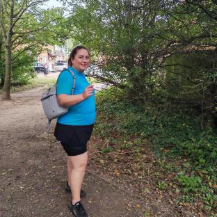 Woman walking on a path, wearing a blue shirt and black shorts.