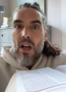 Russell Brand holding a book and speaking.