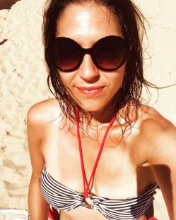 Woman in striped bikini top and sunglasses on a beach.