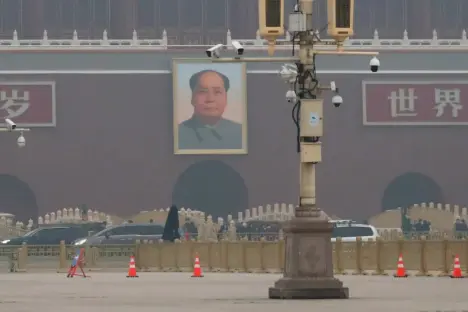 Portrait of Mao Zedong on a wall in Tiananmen Square, with security cameras visible.