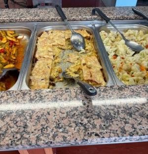 Buffet-style food serving containers with baked casserole, roasted vegetables, and cauliflower.